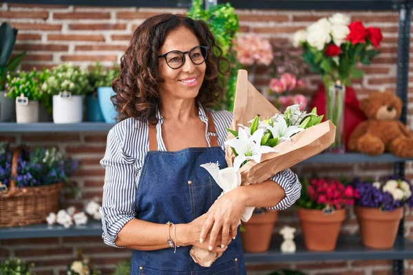 Çiçekçide elinde buket çiçek tutan orta yaşlı bir kadın.