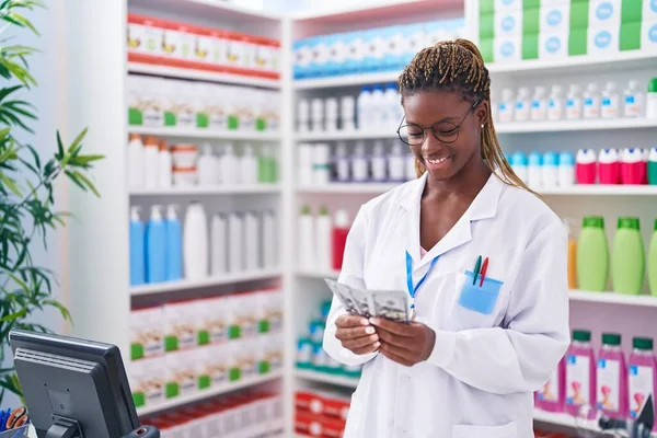 African american woman pharmacist smiling confident counting dollars at pharmacy