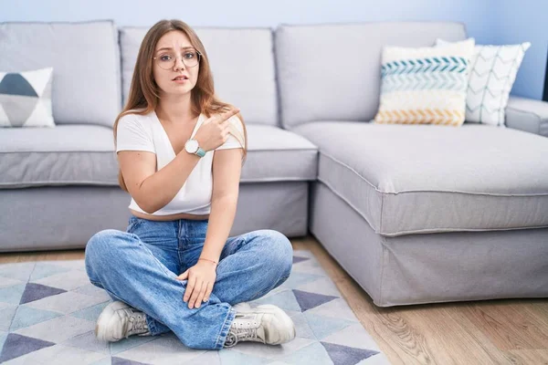 年轻的高加索女人坐在客厅的地板上 用食指 关心和惊讶的表情 把焦虑和紧张放在一边 — 图库照片