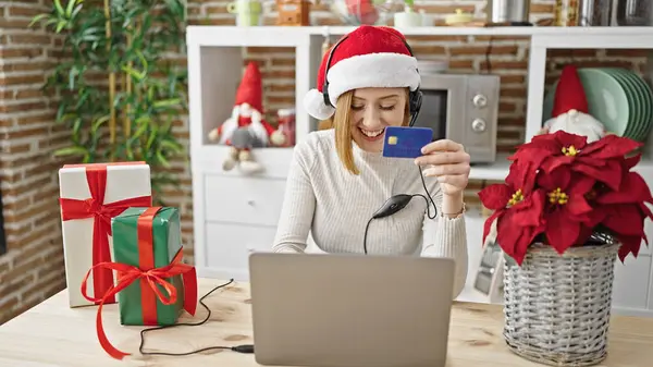 Young blonde woman shopping with laptop and credit card celebrating christmas dancing at dinning room