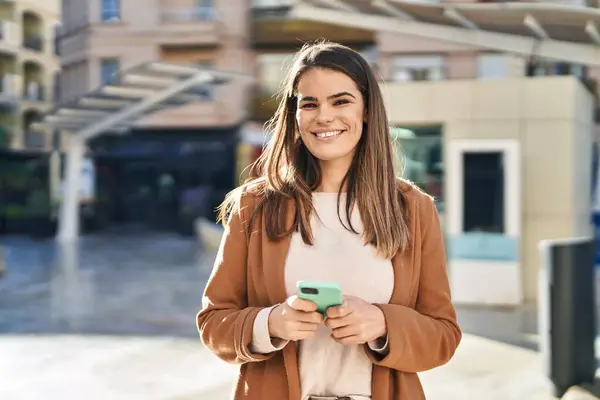 Genç, güzel, İspanyol bir kadın sokakta akıllı telefon kullanarak gülümsüyor.
