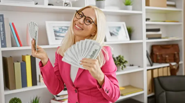 Young blonde woman business worker holding dollars at the office