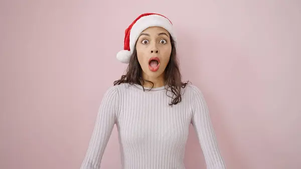 年轻美丽的惊慌失措的女人 带着圣诞帽 披着淡淡的粉色背景 惊讶地面带微笑 — 图库照片