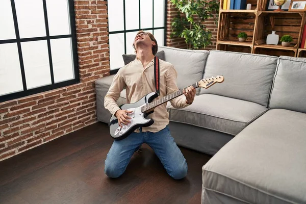 Young caucasian man playing electrical guitar on floor at home