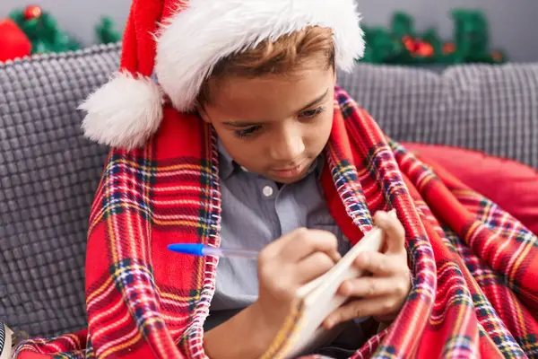 自宅でサンタクロースの手紙を書くクリスマスの帽子をかぶっている愛らしいヒスパニックの少年 — ストック写真