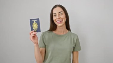 Pasaportu elinde tutan güzel İspanyol kadın mutlu ve pozitif gülümsüyor, başparmağıyla mükemmel bir iş çıkarıyor ve izole edilmiş beyaz arka plan üzerinde onay işareti yapıyor.