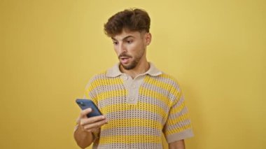 Genç bir Arap adam, sakallı, şaşkın ve şaşkın, akıllı telefonuna bakarken şaşırmış, izole edilmiş sarı bir arka planda mesaj atıyor. Vay canına, bu inanılmaz bir mesaj mı?!