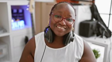 Kendinden emin Afrikalı Amerikalı kadın müzisyen, neşe saçıyor, müzik stüdyosunda kulaklık takıyor.
