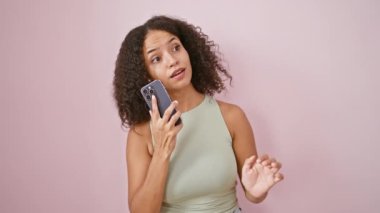 Genç, güzel, İspanyol bir kadın akıllı telefondan konuşuyor izole edilmiş pembe arka planda kutlama yapıyor.