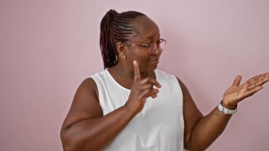 Neşeli Afro-Amerikalı kadın kendine güvenen, mutlu bir şekilde dikilip izole edilmiş pembe arka planda sunum yapıyor. Yetişkinlerin mutluluk ifadesi, parmaklarla kopyalama alanını gösterir.