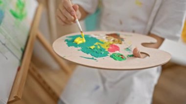 Sevimli sarışın erkek sanatçı kendine güvenerek sandalyede oturuyor, kapalı bir sanat stüdyosunda çizim yapıyor, yaratıcılığı somutlaştırıyor.