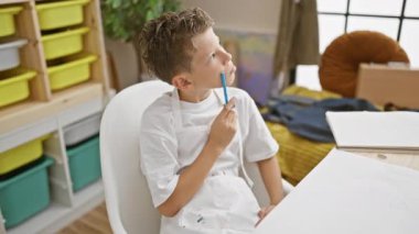 Sevimli sarışın sanatçı, bir sonraki vuruşundan şüphe eden, düşünce stüdyosunda kaybolmuş, elinde boya fırçası, resim sınıfı tuvali ve fikrini bekleyen renkli palet..