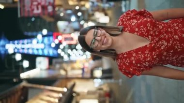Kendine güvenen İspanyol bir kadın, gözlüklü güzel bir esmer, Osaka 'nın şehir sokaklarında neşeyle poz veriyor, gece ışıklarını kaygısız, ışıltılı bir gülümsemeyle kucaklıyor..