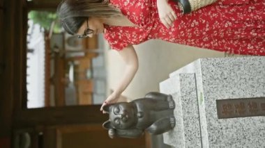 Gözlüklü güzel İspanyol kadın, şansa bel bağlamış, Tokyo 'daki Gothokuji Tapınağı' nın ünlü şanslı kedi heykelinin yanında duruyor.