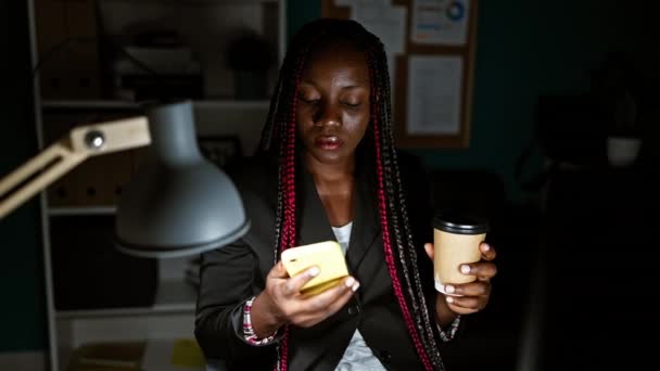 严重的非洲裔美国女性老板大步走向成功 通过智能手机深入工作对话 在黑暗的办公室氛围中喝着浓咖啡 — 图库视频影像