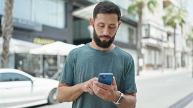 Genç İspanyol adam sokakta akıllı telefon ve kulaklık kullanıyor.