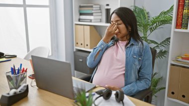 Genç bir kadın iş yerinde stresli, çok çalışan hamile bir iş adamı ofis içi dizüstü bilgisayarla ilgili stresle uğraşıyor..