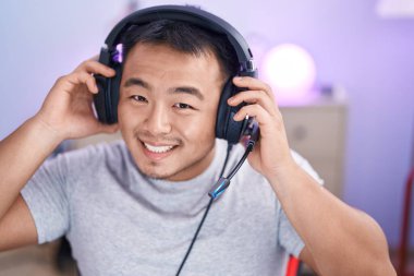 Oyun odasında kulaklık takıp video oyunu oynayan Çinli genç adam.