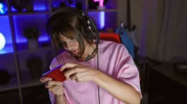 Young beautiful hispanic woman streamer playing video game using smartphone at gaming room