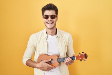 Genç İspanyol adam sarı arka planda ukulele çalıyor ve kahkahalarla gülüyor çünkü komik çılgın bir şaka.. 