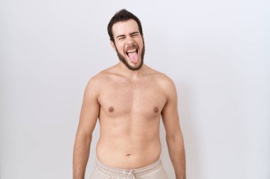 Beyaz arka plan üzerinde tişörtsüz duran İspanyol genç adam komik bir ifadeyle dilini dışarı çıkarıyor. duygu kavramı. 