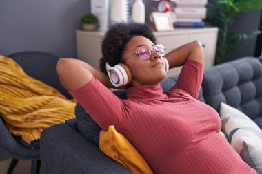 Afro-Amerikalı kadın evdeki kanepede rahatça müzik dinliyor.