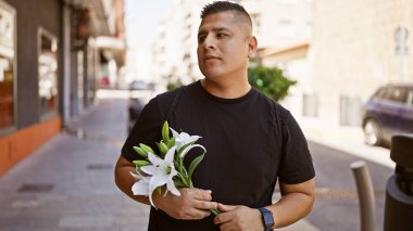 Hip, genç latin adam güneşli bir şehir sokağında bir buket çiçek sallıyor, rahat bir yaşam tarzı olan, modaya uygun bir şekilde.