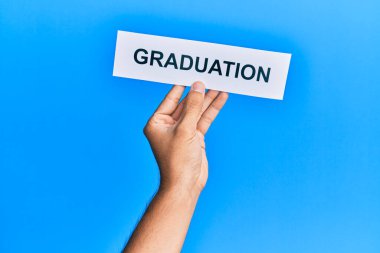 Hand of caucasian man holding paper with graduation word over isolated blue background
