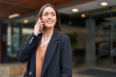 Genç, güzel, İspanyol bir kadın gülümsüyor ve caddede akıllı telefondan konuşuyor.