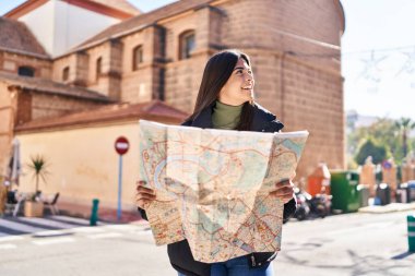 Genç, güzel, İspanyol bir kadın gülümsüyor. Elinde şehir haritası tutuyor.