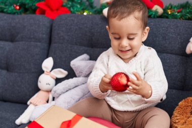 Sevimli İspanyol bebek elinde noel balosu tutarak evdeki kanepede oturuyor.