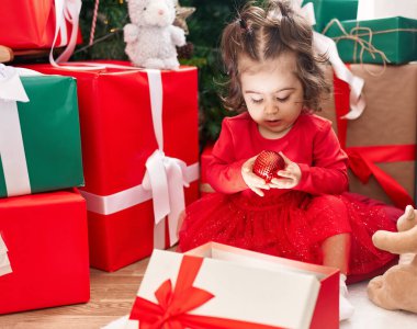 Sevimli İspanyol kız hediyesini açıyor. Evdeki Noel ağacının yanında oturuyor.
