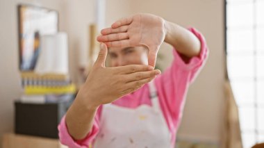 Bir sanat stüdyosunda, gülümseyen genç bir İspanyol kadın, tutkulu bir sanatçı, tuval ve resim sehpası arasında fotoğraf el hareketleriyle bir resmi güzel çerçeveler.