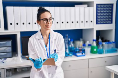 Young caucasian woman scientist smiling confident writing on notebook at laboratory