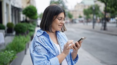 Genç ve güzel İspanyol kadın mutlu bir şekilde gülümsüyor Viyana sokaklarında akıllı telefon kullanıyor.