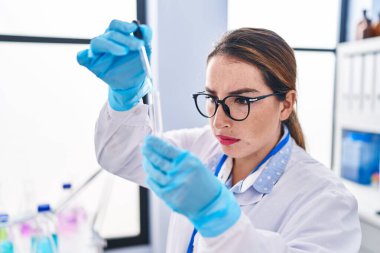 Genç ve güzel İspanyol bilim kadını laboratuarda test tüpüne sıvı döküyor.