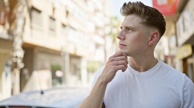 Sakallı, yakışıklı, beyaz bir adam, güneşli bir sokakta şüpheyle duruyordu, derin düşüncelere dalmış, ciddi ama rahat bir şehir yaşam tarzına odaklanmış..