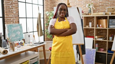 Kendine güvenen Afrikalı Amerikalı kadın sanatçı, gülümsüyor, sanat stüdyosunda kollarını kavuşturuyor.