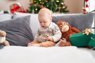 Evdeki gevşek yüzlü, Noel ağacının yanındaki kanepede oturan sevimli beyaz bebek.