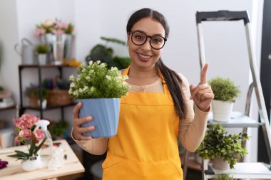 Çiçekçi dükkanında çalışan genç bir Arap kadın elinde saksıyla gülümsüyor. 