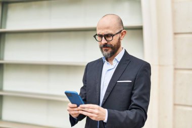 Genç kel iş adamı caddede akıllı telefon kullanıyor.