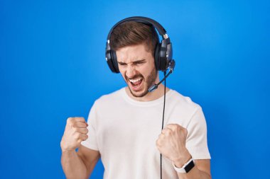 Sakallı, müzik dinleyen, kulaklık takan, mutlu ve heyecanlı İspanyol bir adam kolları havada, gülümseyen ve başarı çığlıkları atan, kazanan bir jest yapıyor. kutlama konsepti. 