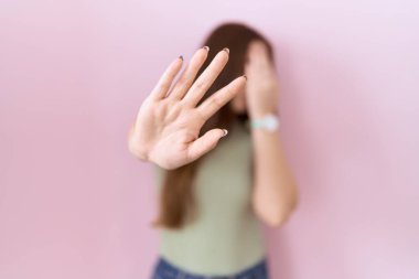 Güzel esmer kadın pembe arka planda duruyor ellerle gözleri örtüyor ve üzgün ve korku ifadeleriyle dur hareketi yapıyor. utangaç ve olumsuz kavram. 