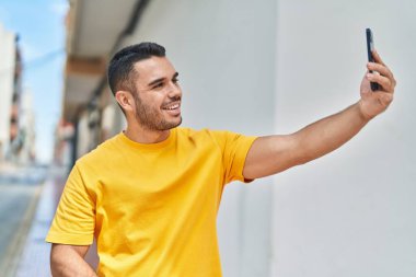 Genç İspanyol adam gülümsüyor. Sokakta akıllı telefonun yanında özçekim yapıyor.