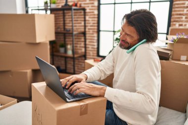 Orta yaşlı bir adam yeni evinde bilgisayarla konuşuyor.