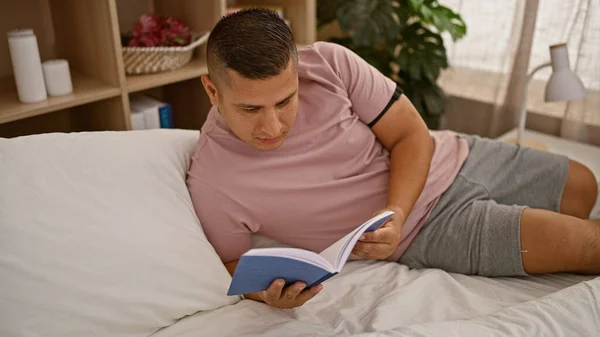 ベッドルームのベッドに横たわる本を読む若いラテン人の男 — ストック写真