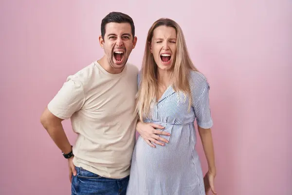 Casal Jovem Esperando Bebê Sobre Fundo Rosa Irritado Louco Gritando — Fotografia de Stock
