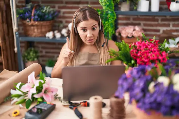 Young blonde woman working at florist shop doing video call smiling with an idea or question pointing finger with happy face, number one