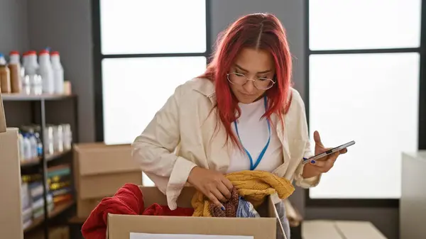 Посвящается Молодой Рыжей Волонтерше Проверяет Пожертвования Одежду Смартфона Благотворительном Центре — стоковое фото