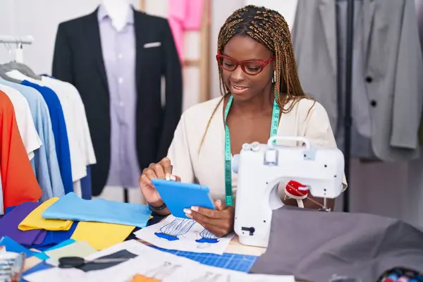 African american woman tailor smiling confident using touchpad at tailor shop